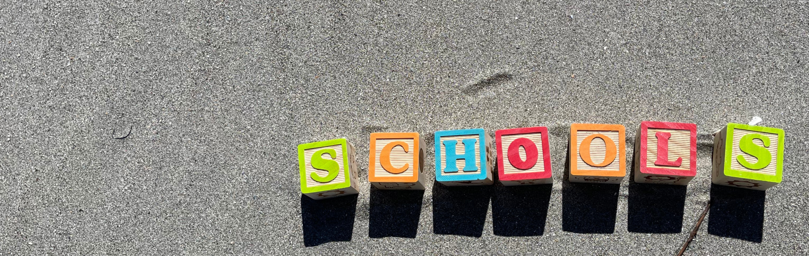 Letter blocks spelling out 'schools' in the sand.